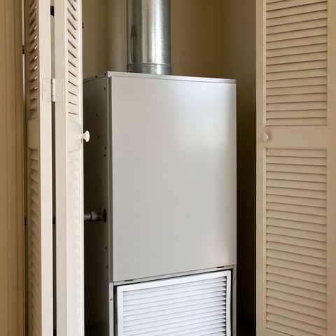 A gas furnace in a hallway closet with its louvered doors folded open